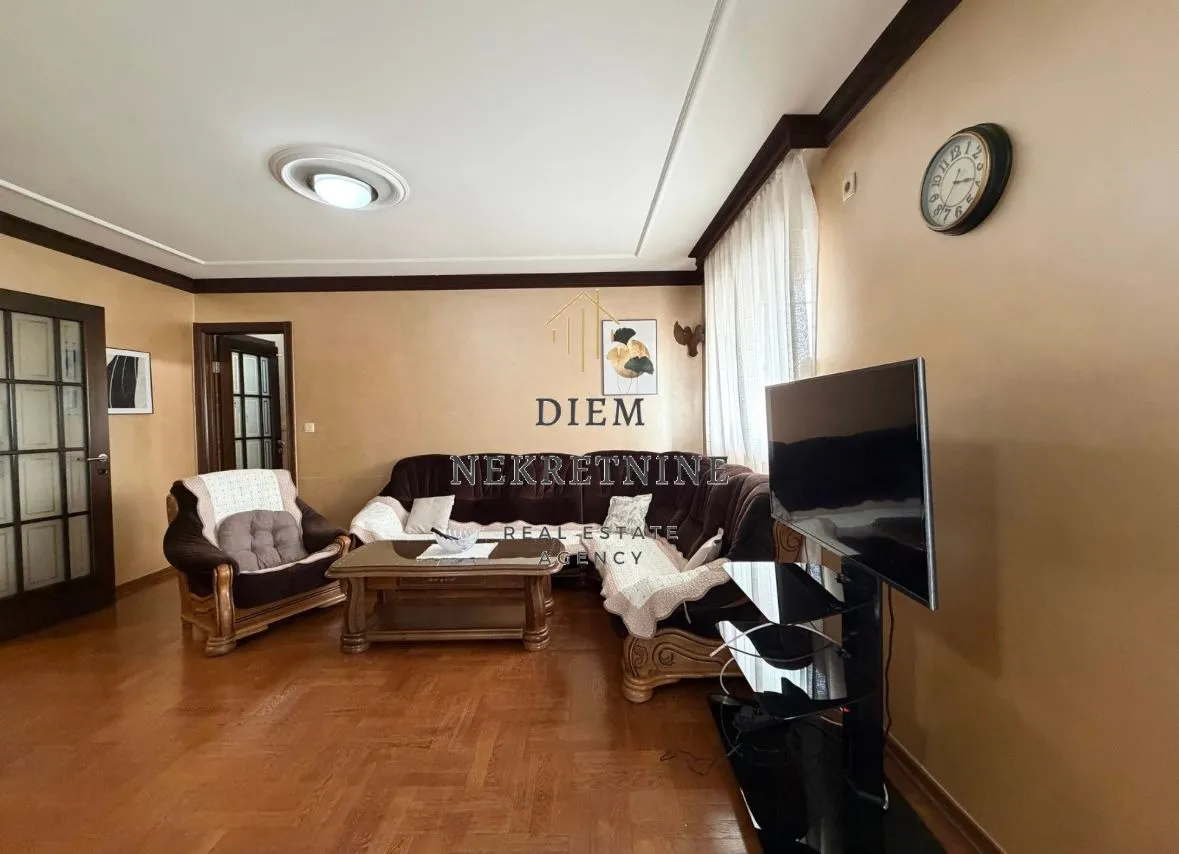 Prostrana dnevna soba sa garniturom, stočićem i televizorom.