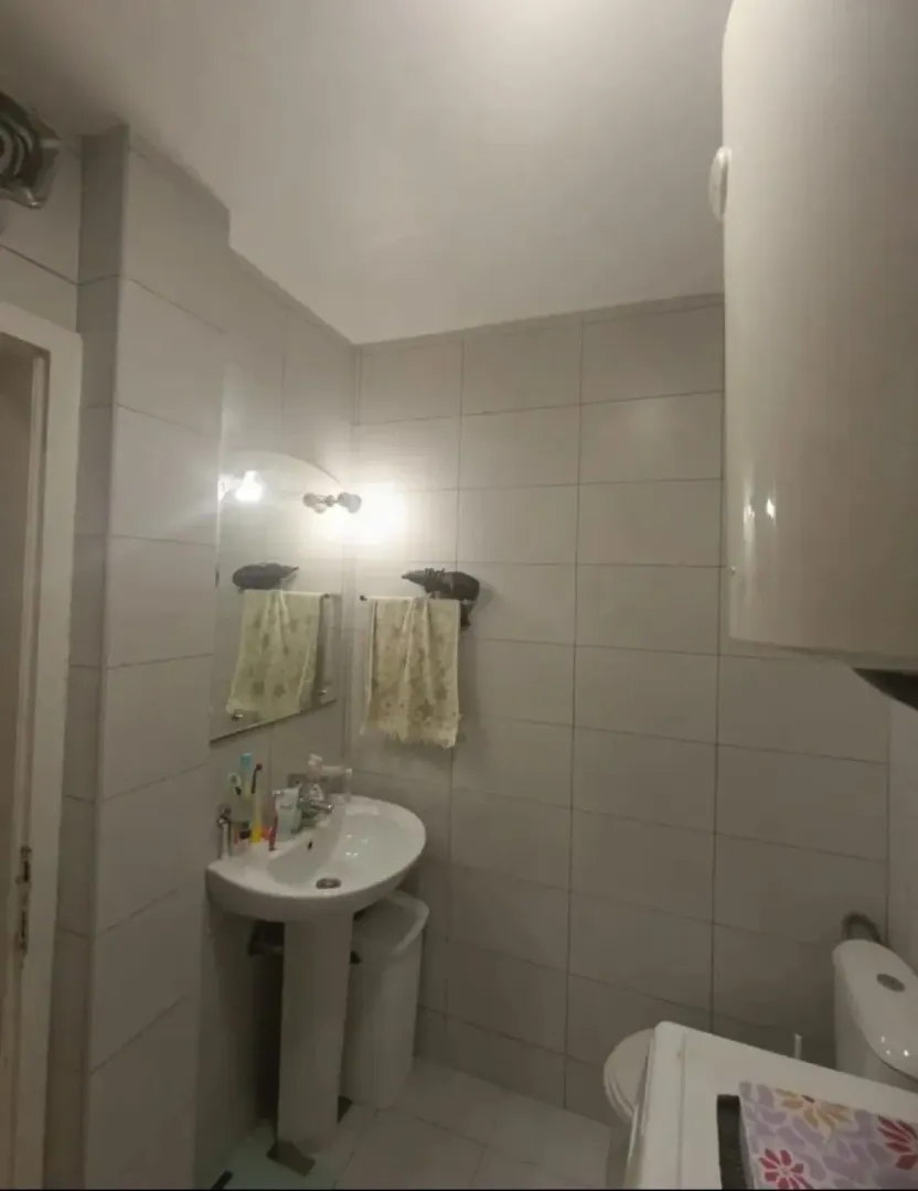 Manje kupatilo obloženo svijetlim pločicama sa umivaonikom i wc šoljom.