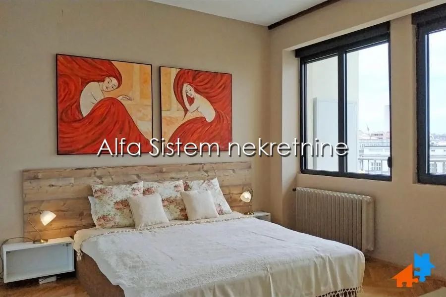 Nameštena spavaća soba sa bračnim krevetom i umetničkim slikama na zidu.