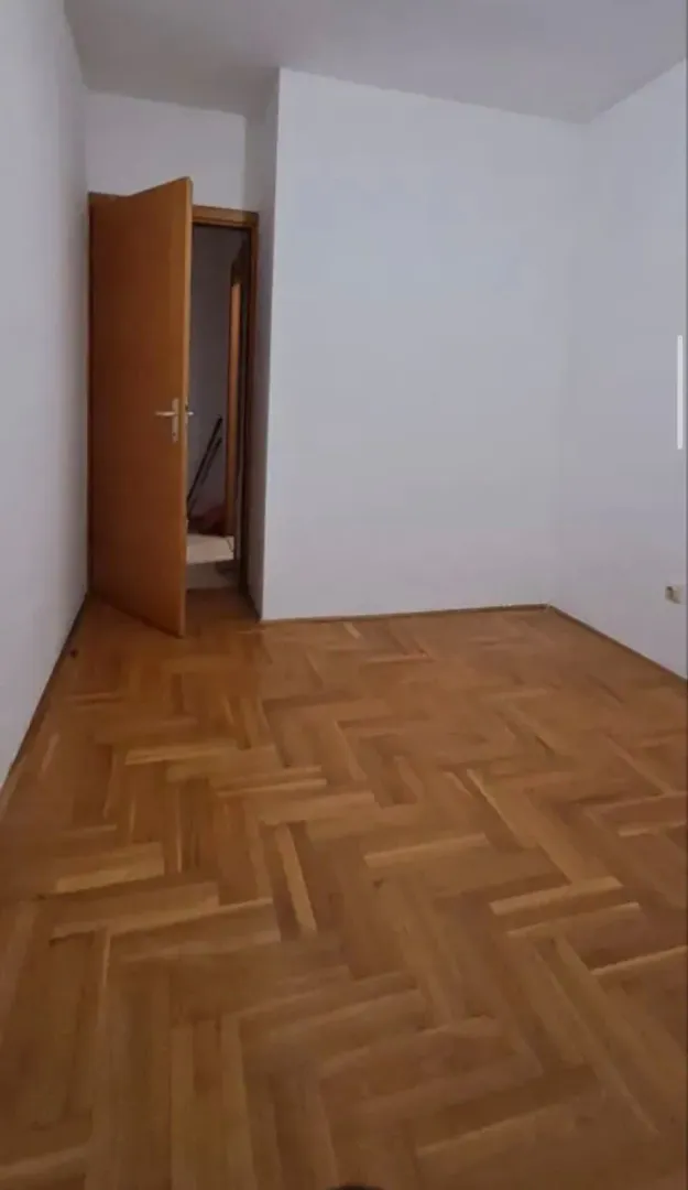Prazna soba sa parketom i otvorenim drvenim vratima.