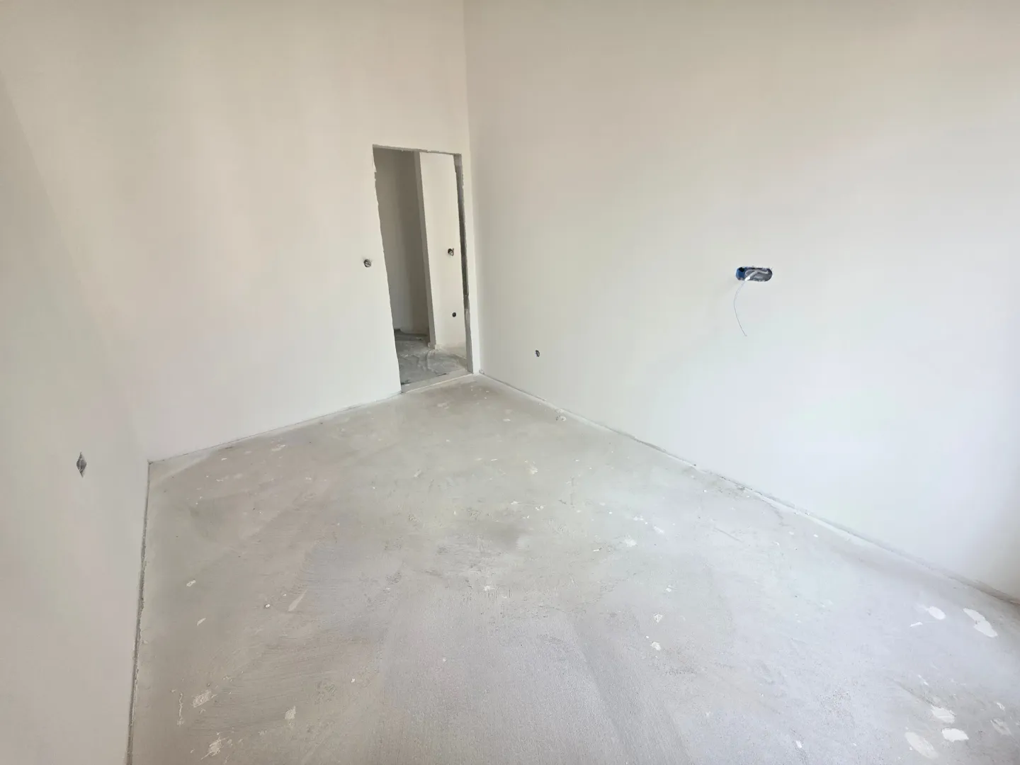Prazna prostorija u novogradnji sa bijelim zidovima i grubim podom.