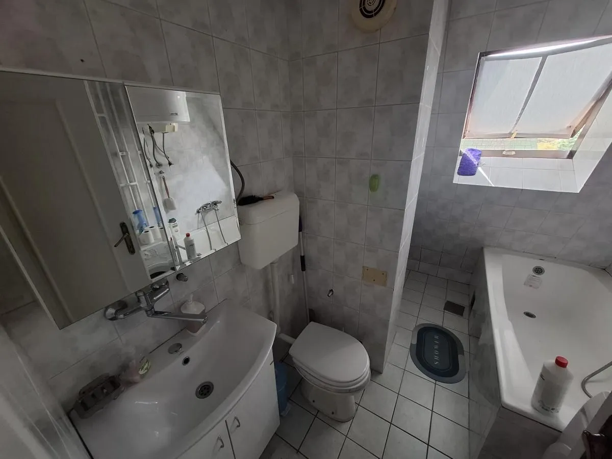 Kupatilo opremljeno umivaonikom, ormarićem sa ogledalom, toaletom i kadom.