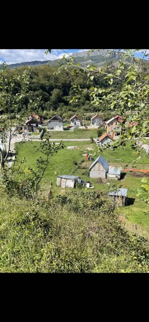 Pogled na kuće i prostrane zelene livade okružene šumom i planinama.