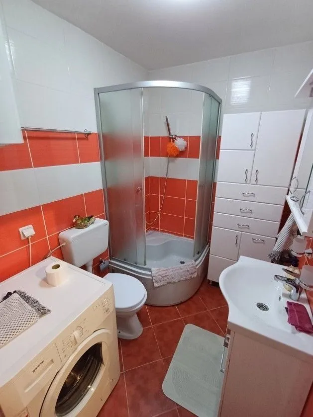 Kupatilo sa tuš kabinom, veš mašinom i narandžastim pločicama.