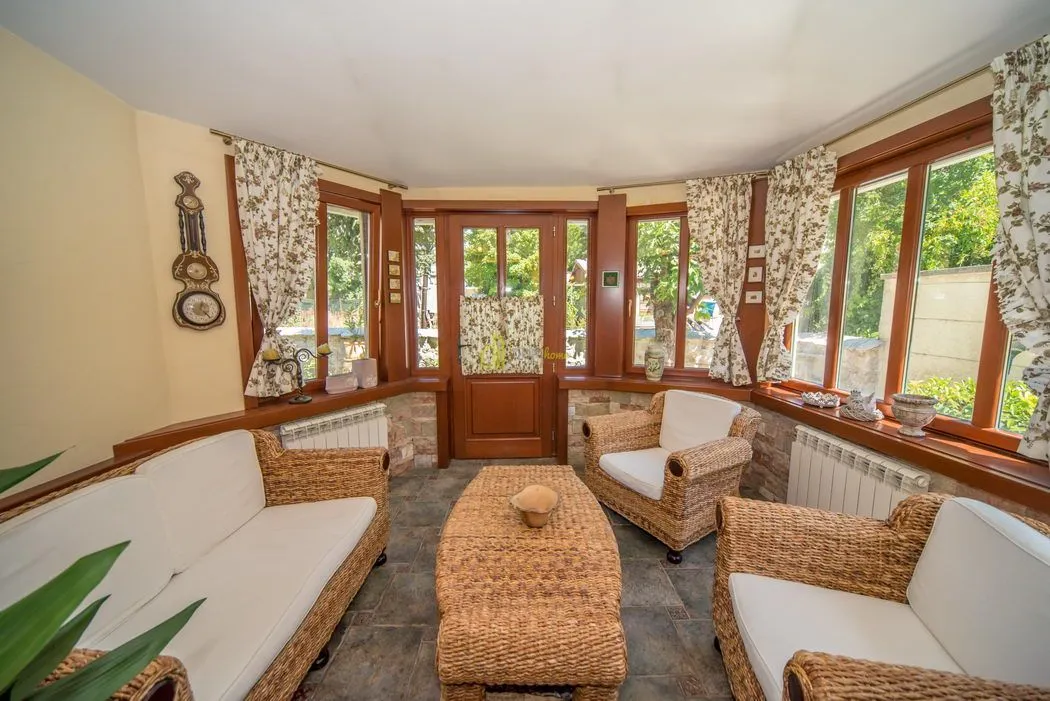 Living room with wicker furniture and large windows overlooking greenery.