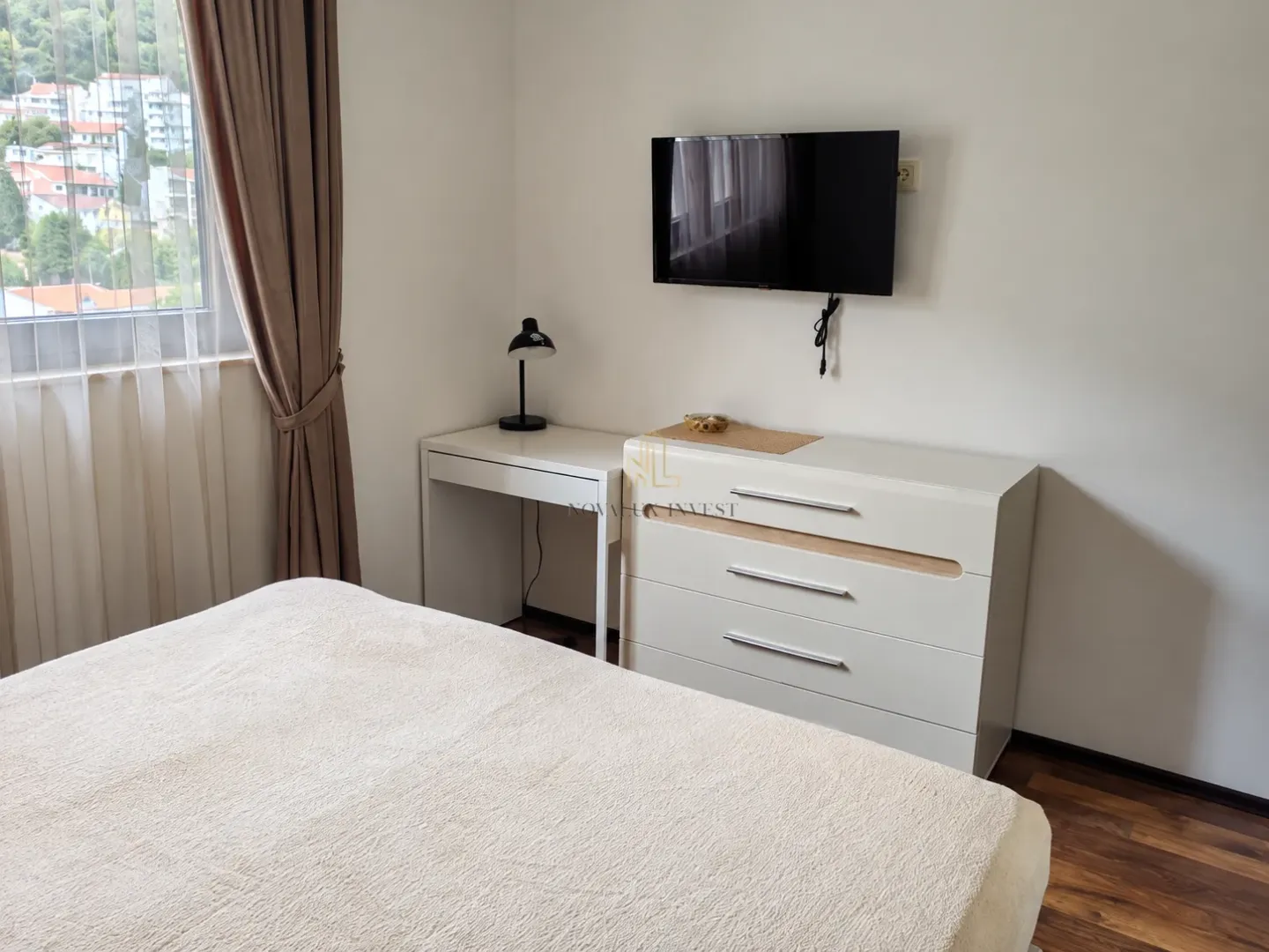 Bedroom with a bed, dresser, desk, and wall-mounted TV.