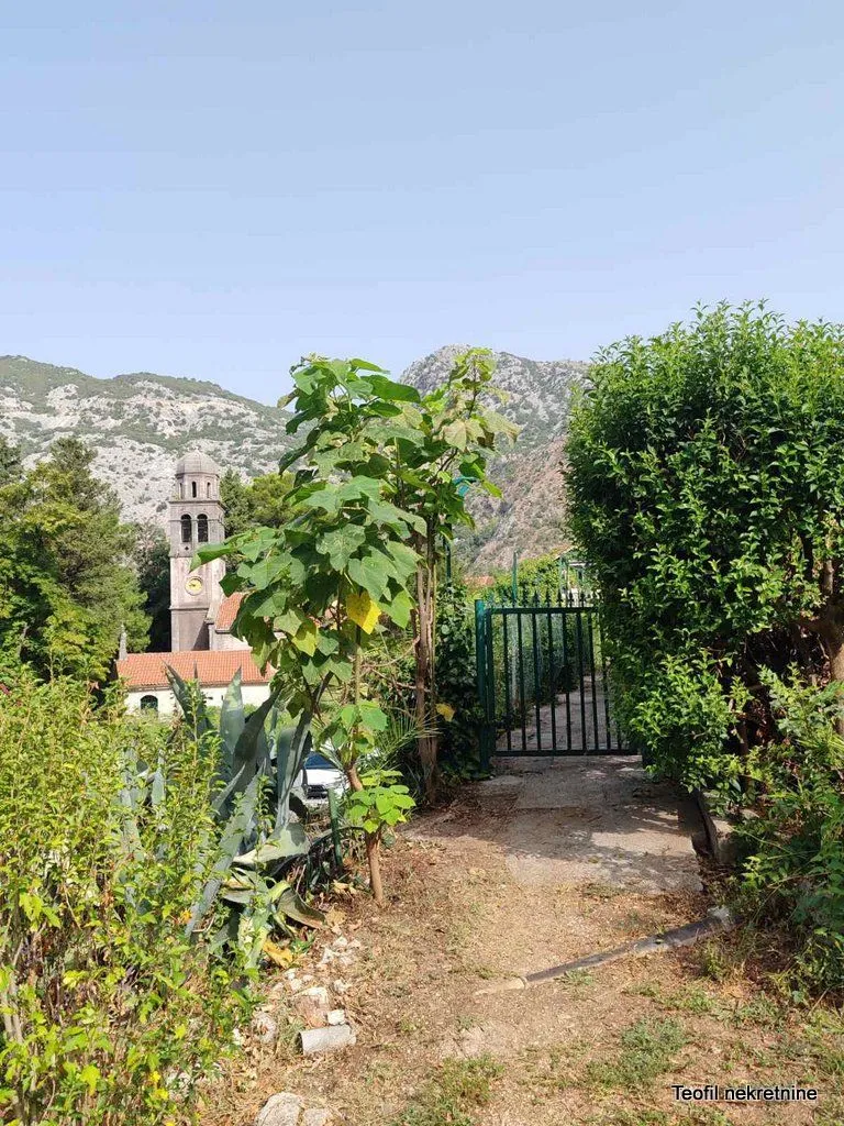 Zeleno dvorište sa stazom, kapijom i pogledom na okolni pejzaž i crkvu.