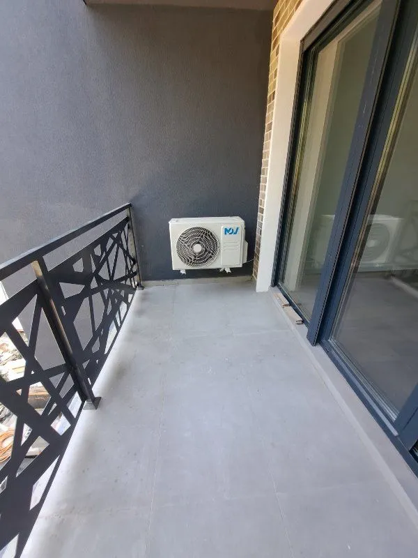 Manji balkon sa metalnom ogradom i spoljnom jedinicom klima uređaja.