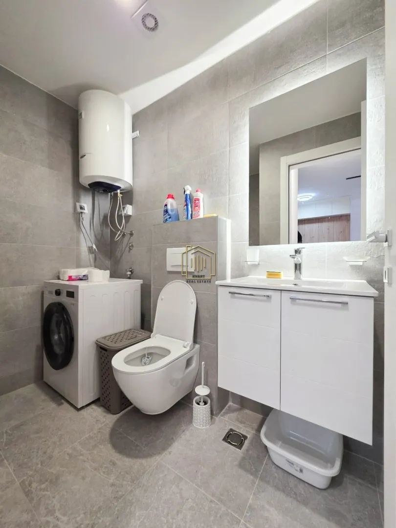 Moderno opremljeno kupatilo sa veš mašinom, wc šoljom i umivaonikom.