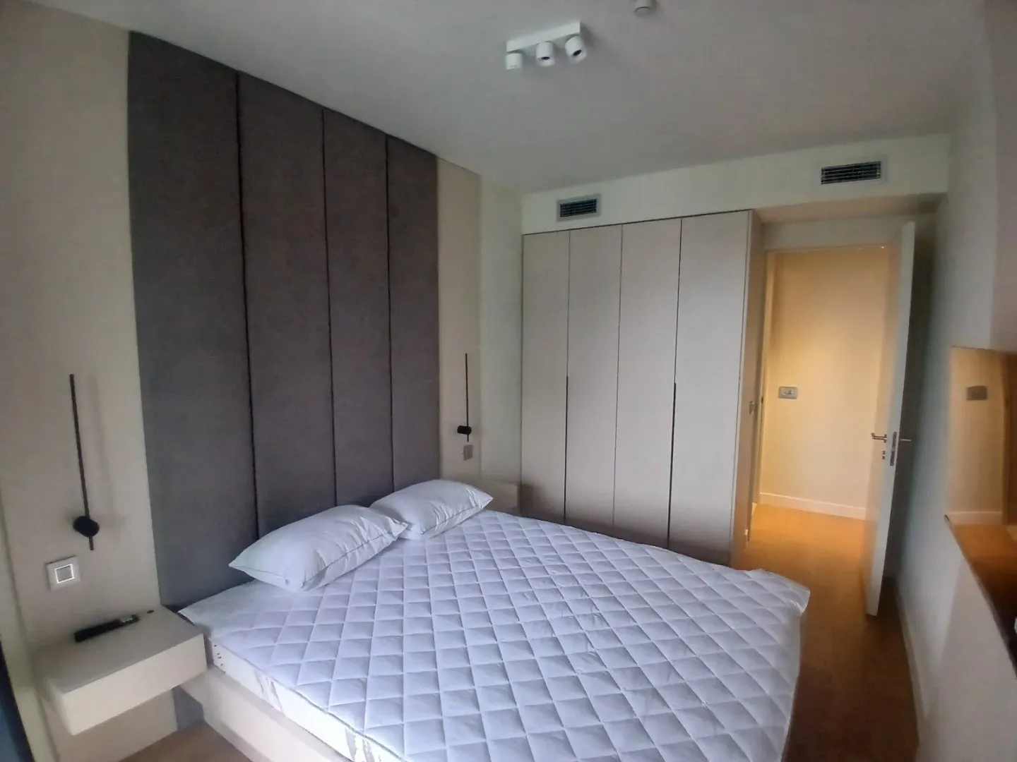 Moderna spavaća soba sa bračnim krevetom, tapaciranim uzglavljem i ugradnim ormarom.