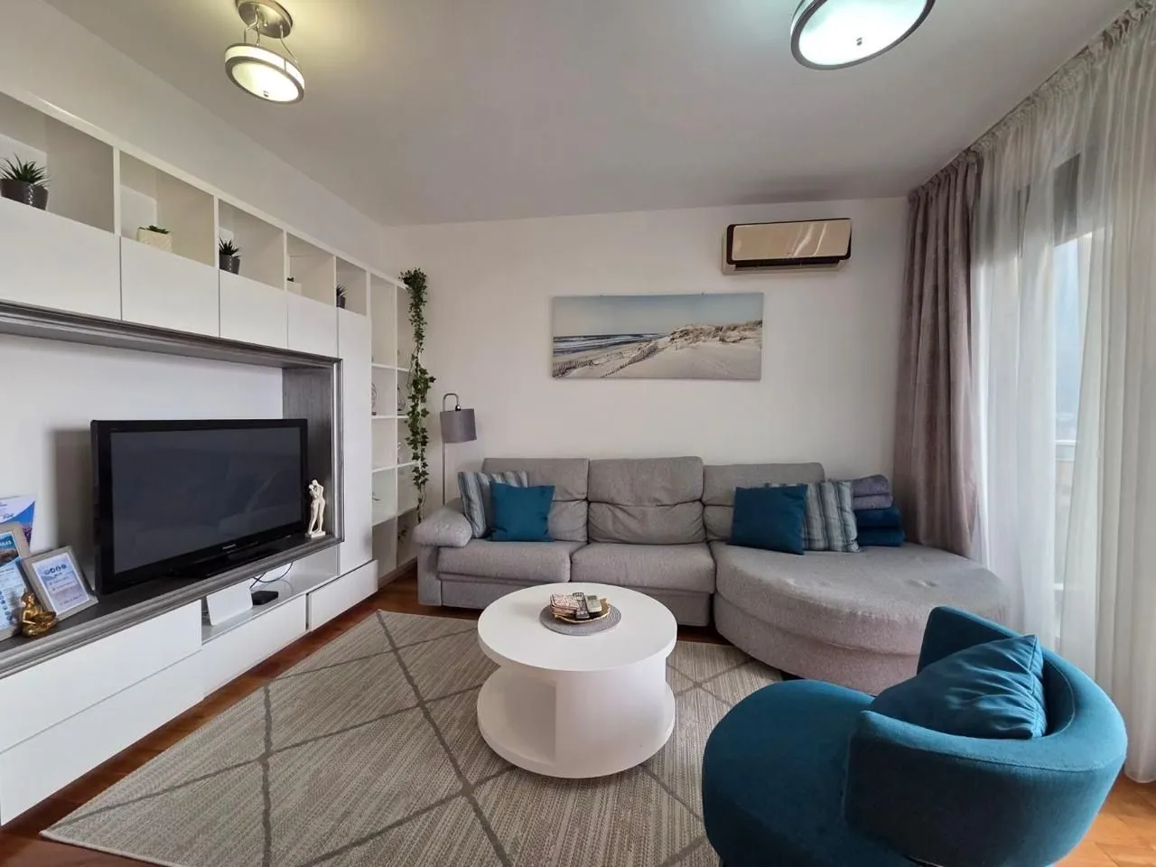 Furnished living room with a corner sofa, TV, and white shelving units.