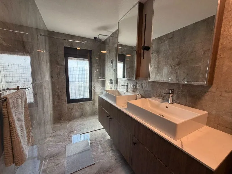 Modern bathroom with double sinks, large mirrors, and a walk-in shower.