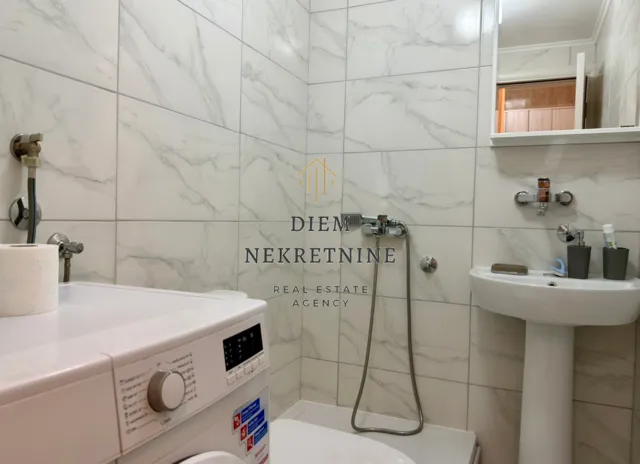 Small bathroom with white marble tiles, washbasin and washing machine.