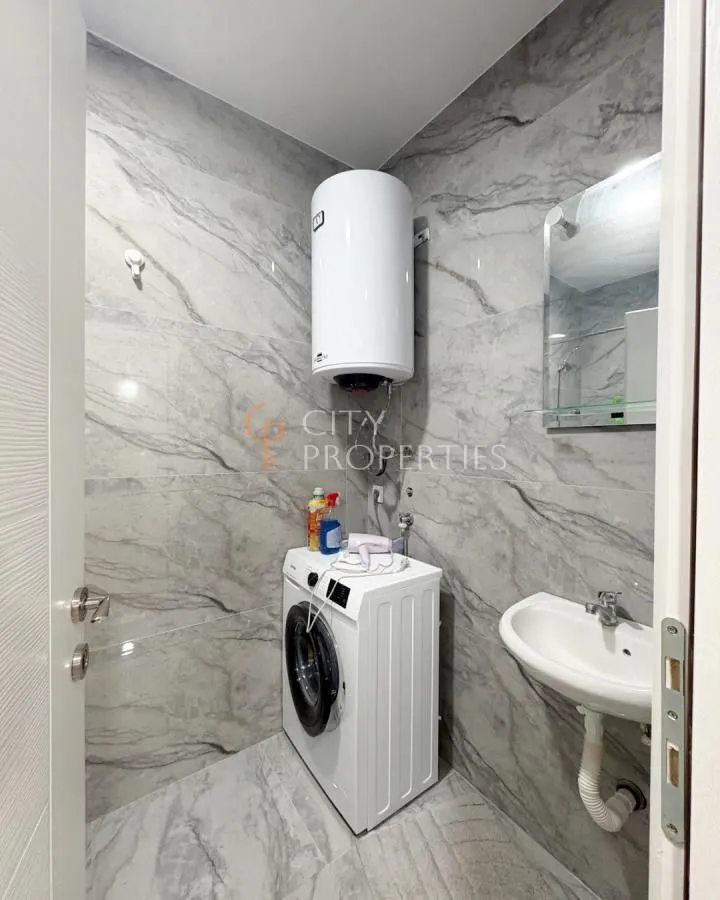 Bathroom with marble-effect tiles, washing machine, sink and water heater.