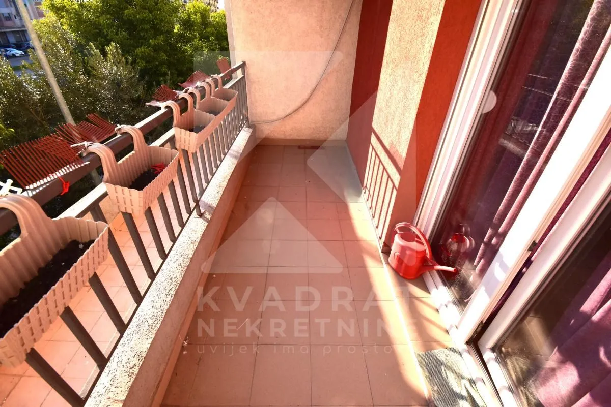 Dugi balkon sa metalnom ogradom i pogledom na zelenilo.