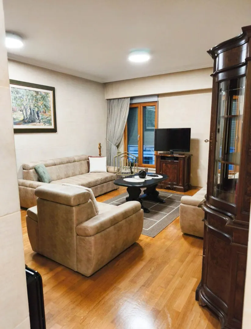 Living room furnished with a sofa set, coffee table, television, and wooden furniture.