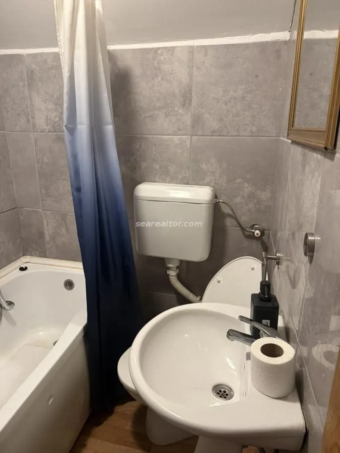 Bathroom lined with grey tiles featuring a bathtub, washbasin, and toilet.