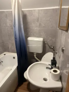 Bathroom lined with grey tiles featuring a bathtub, washbasin, and toilet. - image 8