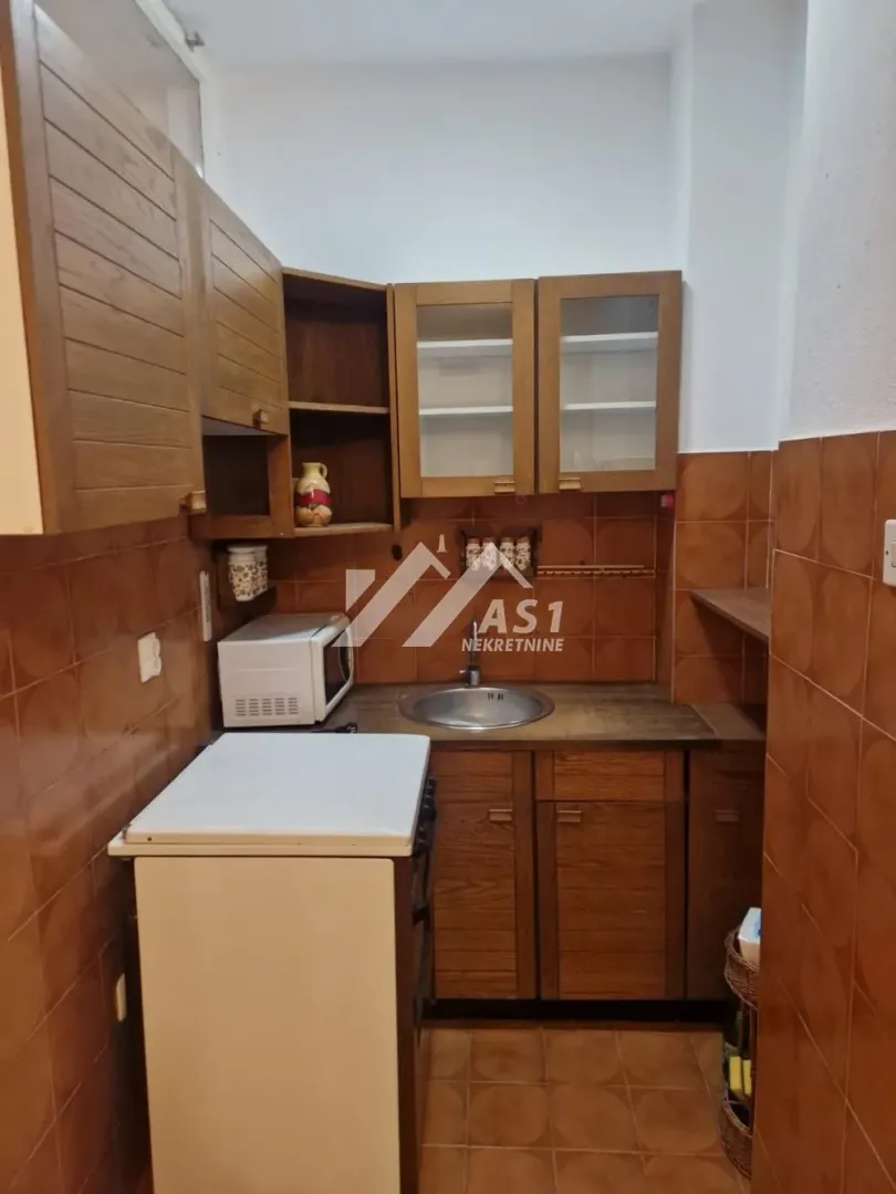 Smaller kitchen with wooden units and brown tiles.