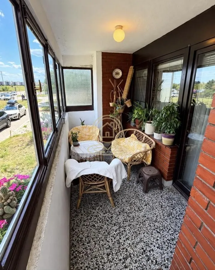 Enclosed balcony with seating furniture and houseplants.