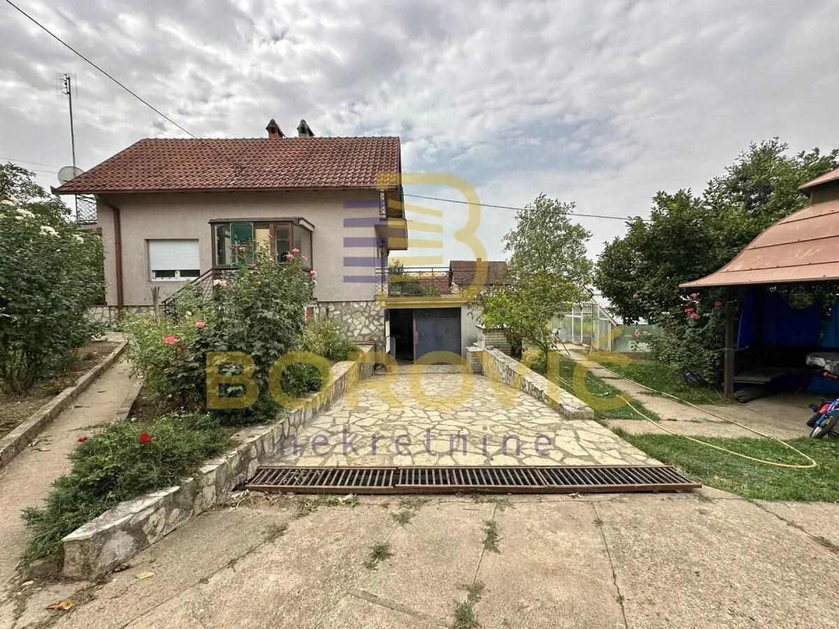 Pogled na dvorište i fasadu kuće sa uređenim prilazom i zelenilom.