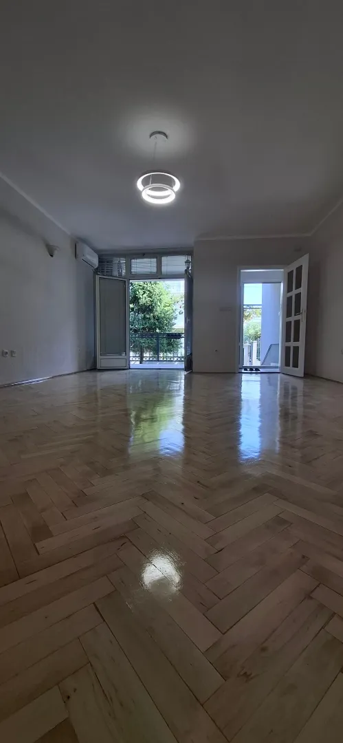 Prazna soba sa drvenim parketom i izlazom na terasu.