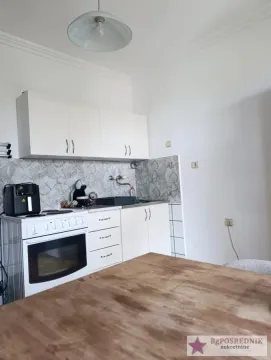 Manja kuhinja sa belim elementima i trpezarijskim stolom u prvom planu. - image 5