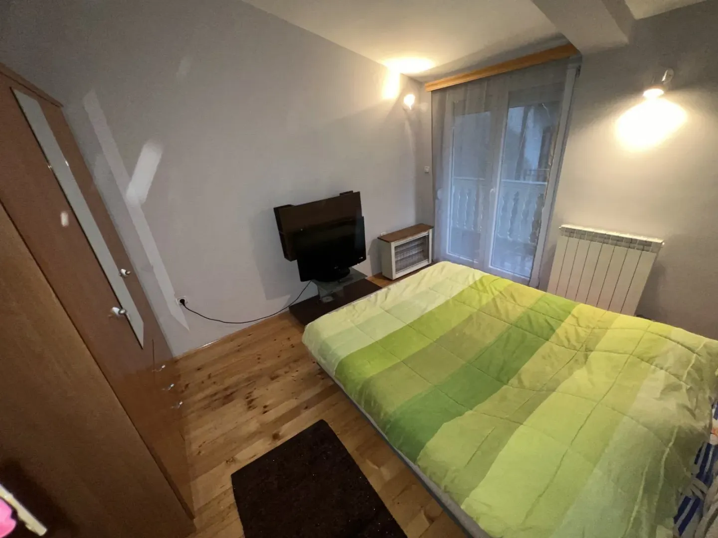 Spavaća soba sa bračnim krevetom, ormarom i izlazom na balkon.
