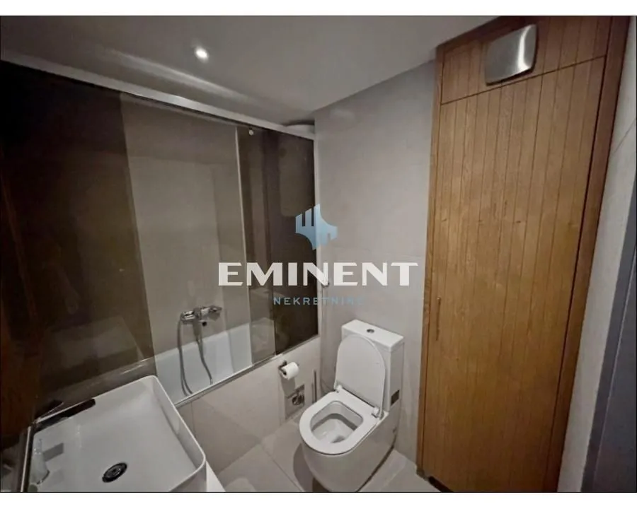 Moderno opremljeno kupatilo sa tuš kabinom, umivaonikom, wc šoljom i drvenim ormarićem.