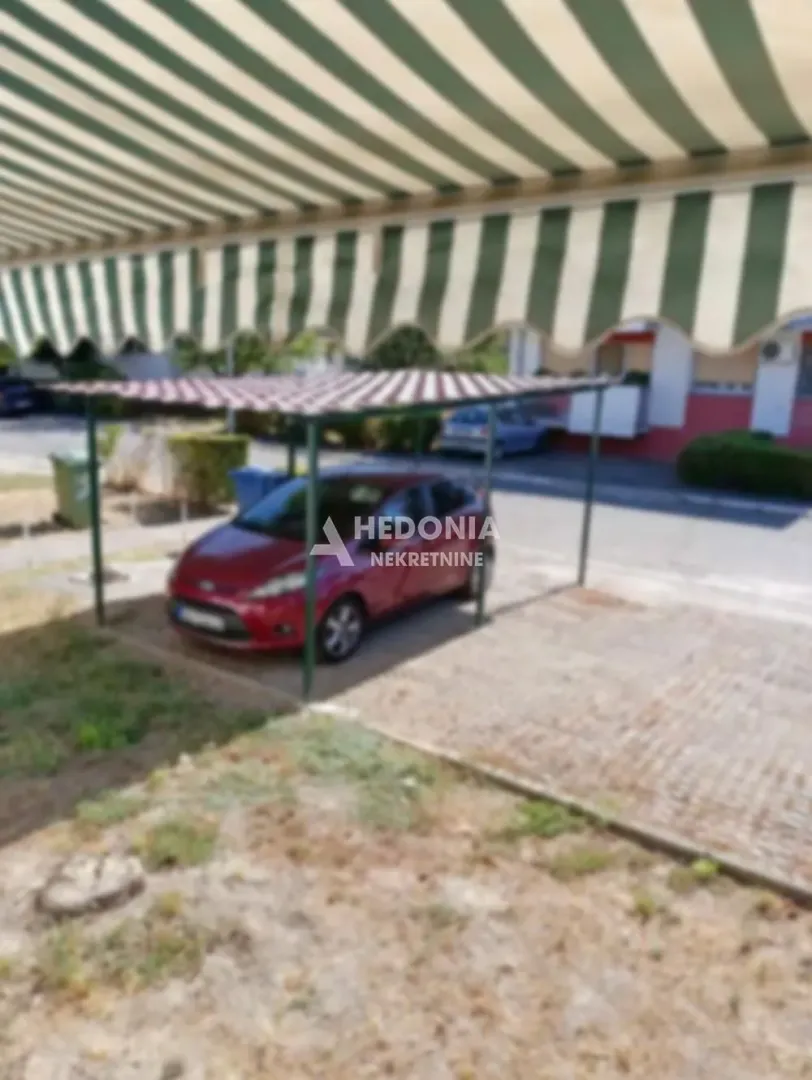 Natkriveni parking prostor sa parkiranim automobilom u dvorištu zgrade.
