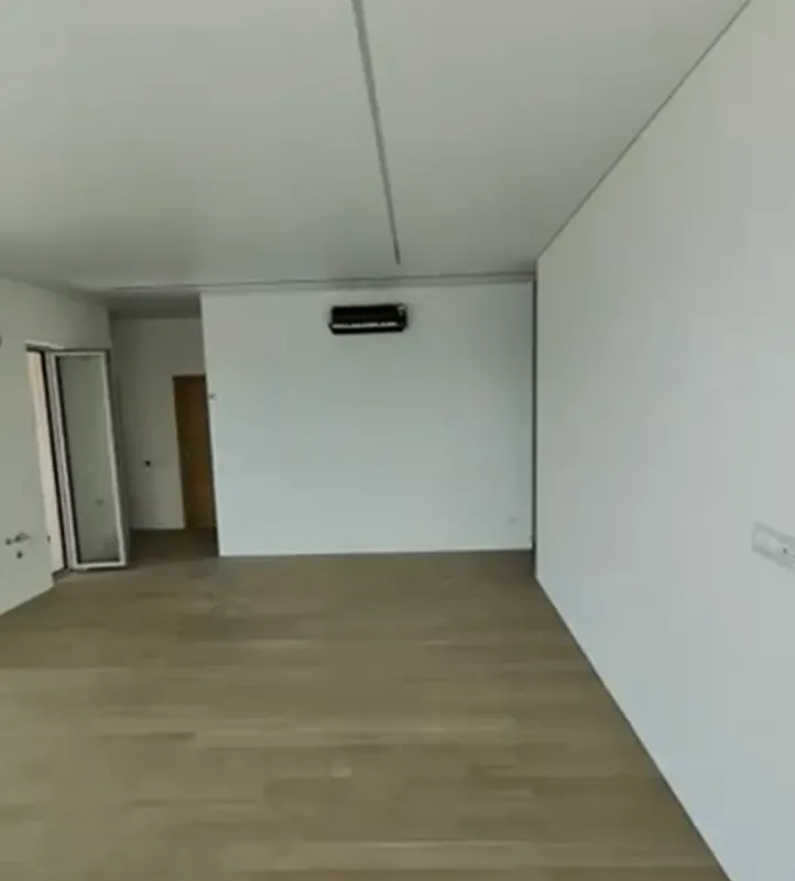 Prazna soba sa bijelim zidovima, drvenim podom i klima uređajem.
