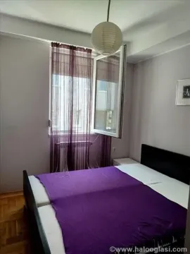 Spavaća soba sa bračnim krevetom i prozorom sa ljubičastim zavesama. - image 10