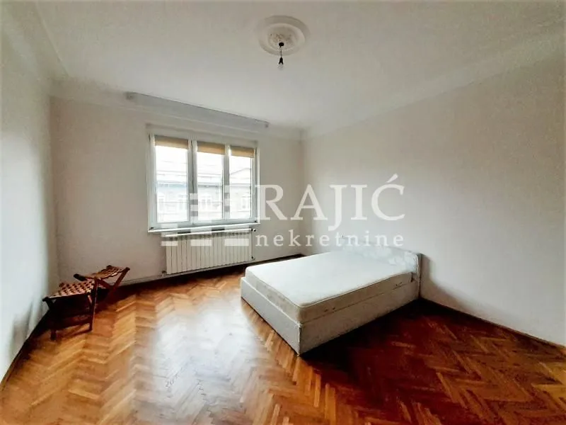 Empty bedroom with a bed and wooden parquet flooring.