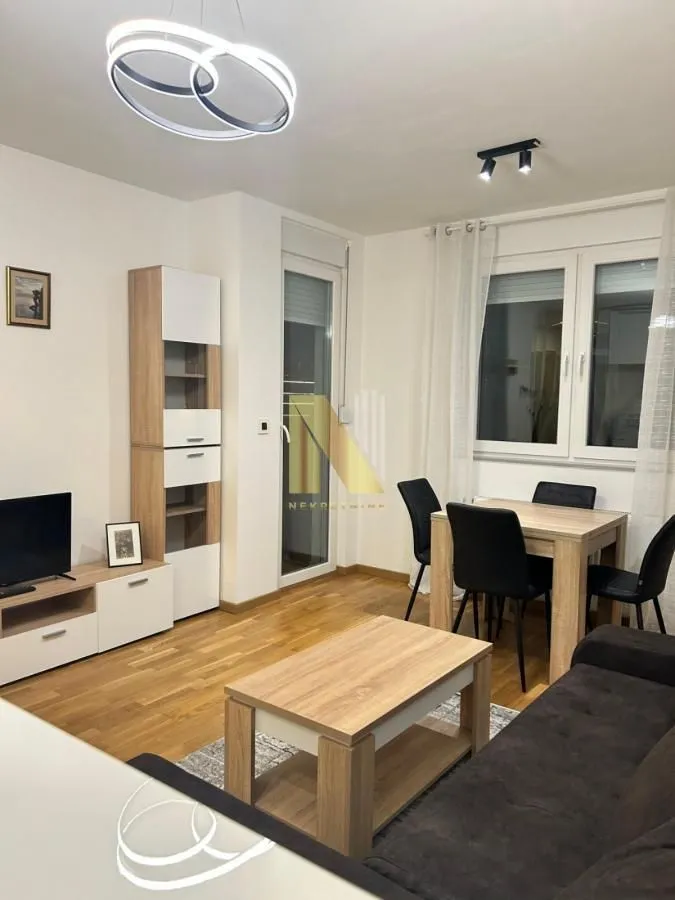 Dnevna soba sa garniturom, TV komodom i trpezarijskim stolom.