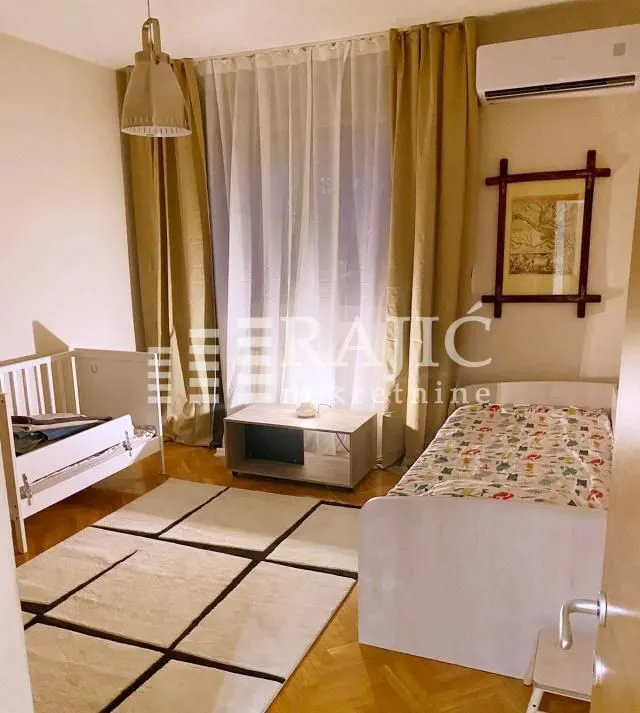 Children's bedroom with two beds, a rug, and a large window.