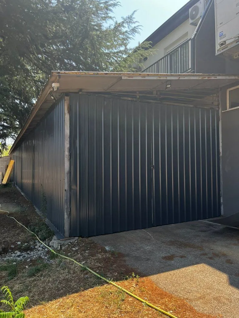 Exterior view of an outbuilding with metal doors in the yard.