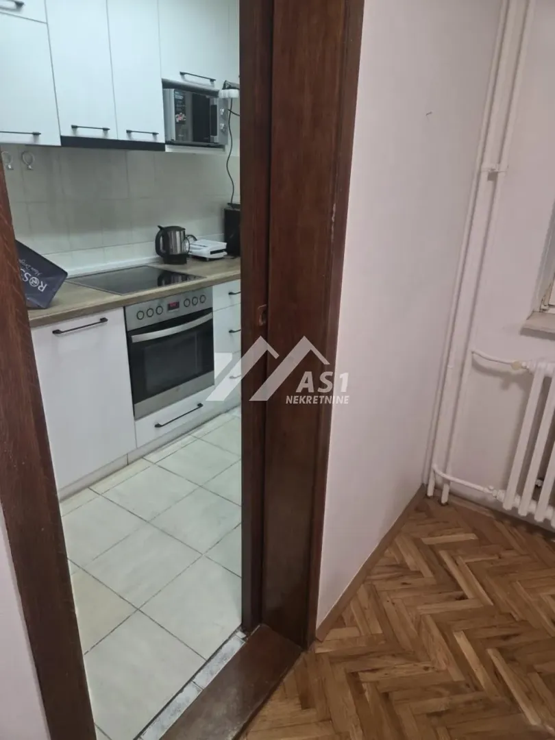Pogled iz hodnika na manju kuhinju sa belim elementima.