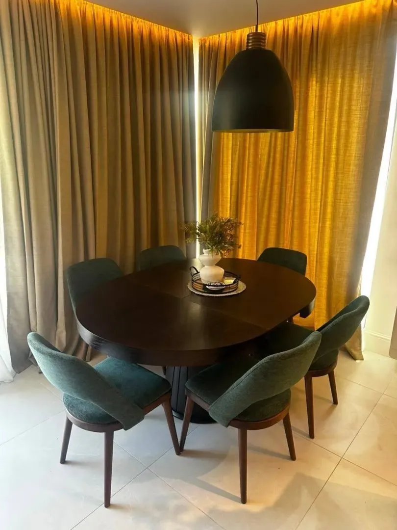 Dining area with a round table and green chairs in front of a window with yellow curtains.