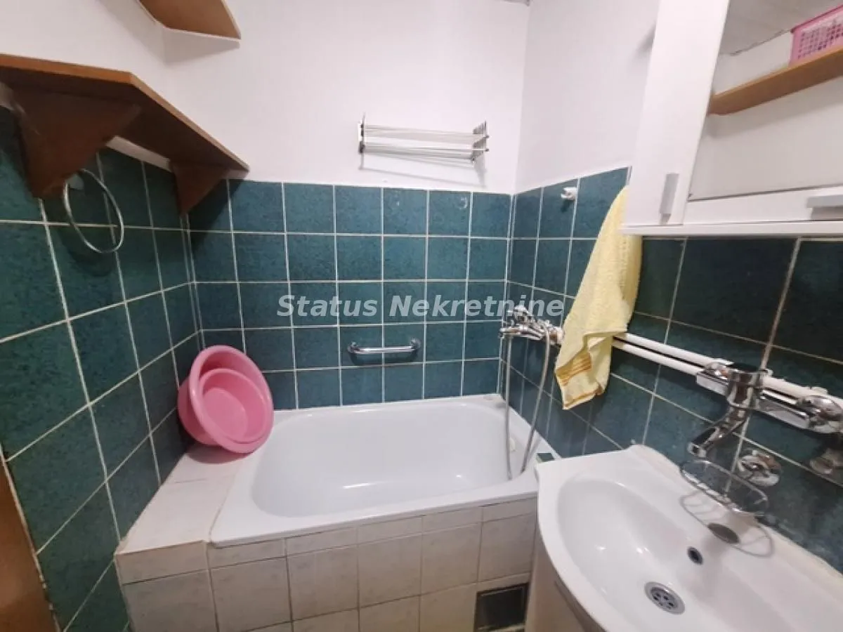 Manje kupatilo sa kadom, umivaonikom i zelenim zidnim pločicama.
