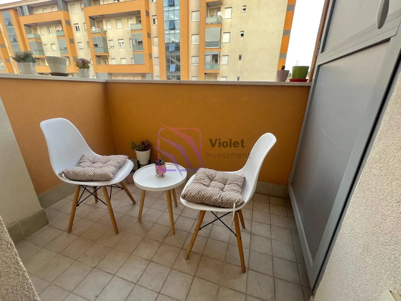 Small furnished balcony with a table, two chairs, and a building view.