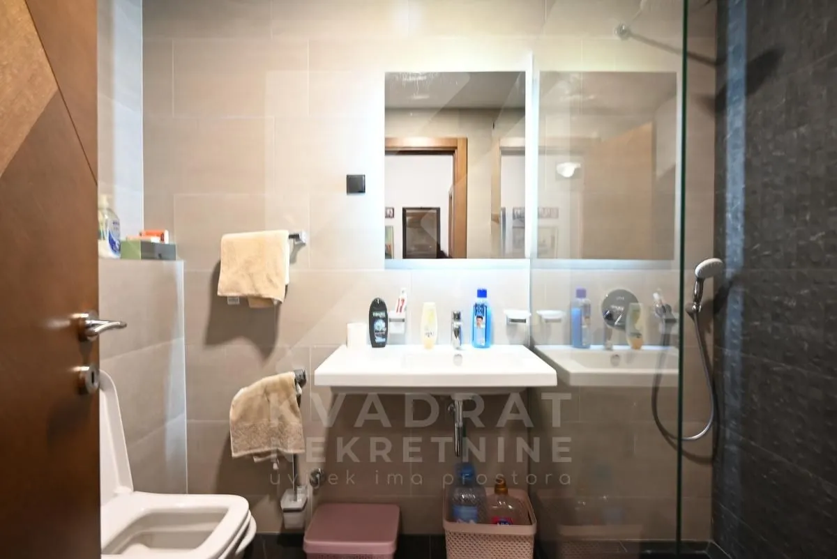 Savremeno opremljeno kupatilo sa umivaonikom, ogledalom i tuš kabinom.