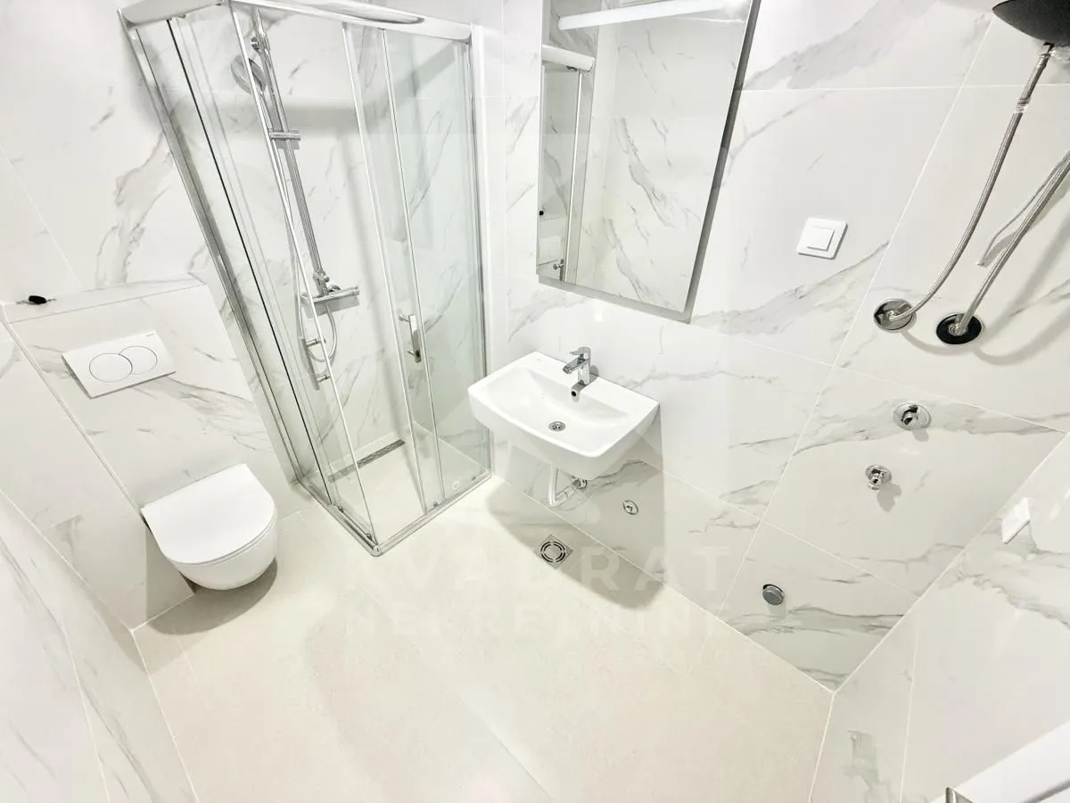 Modern bathroom with a shower enclosure, washbasin, and wall-hung toilet with marble-look tiles.