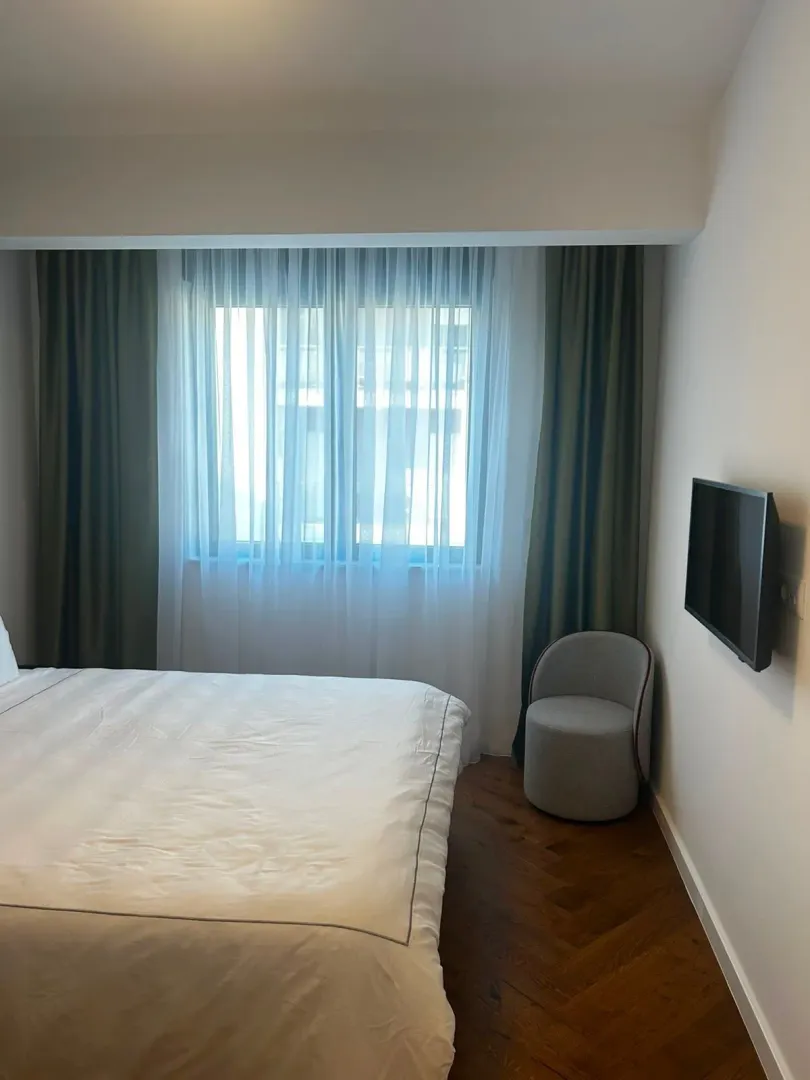 Spavaća soba sa bračnim krevetom, foteljom i zidnim televizorom.
