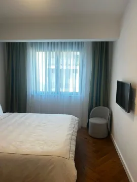 Spavaća soba sa bračnim krevetom, foteljom i zidnim televizorom. - image 9