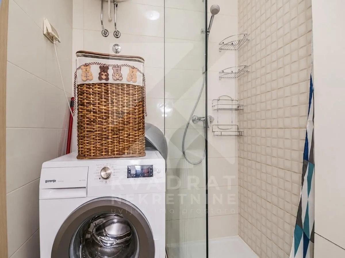 Bathroom with a shower cabin, washing machine, and wicker laundry basket.