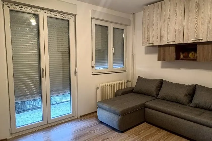 Small living room with a sectional sofa, wall cabinets, and balcony doors.