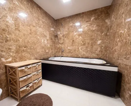 Bathroom tiled with marble finishes featuring a corner bathtub and a wooden storage unit. - image 14