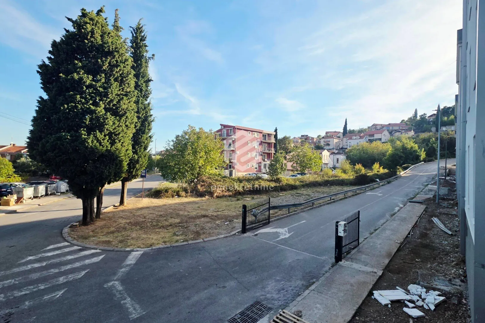 Pogled na prilaz zgradi, ulicu i okolno zelenilo.