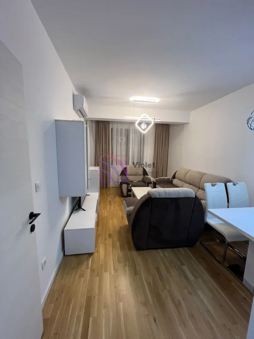 Dnevna soba sa garniturom, TV komodom i trpezarijskim stolom.