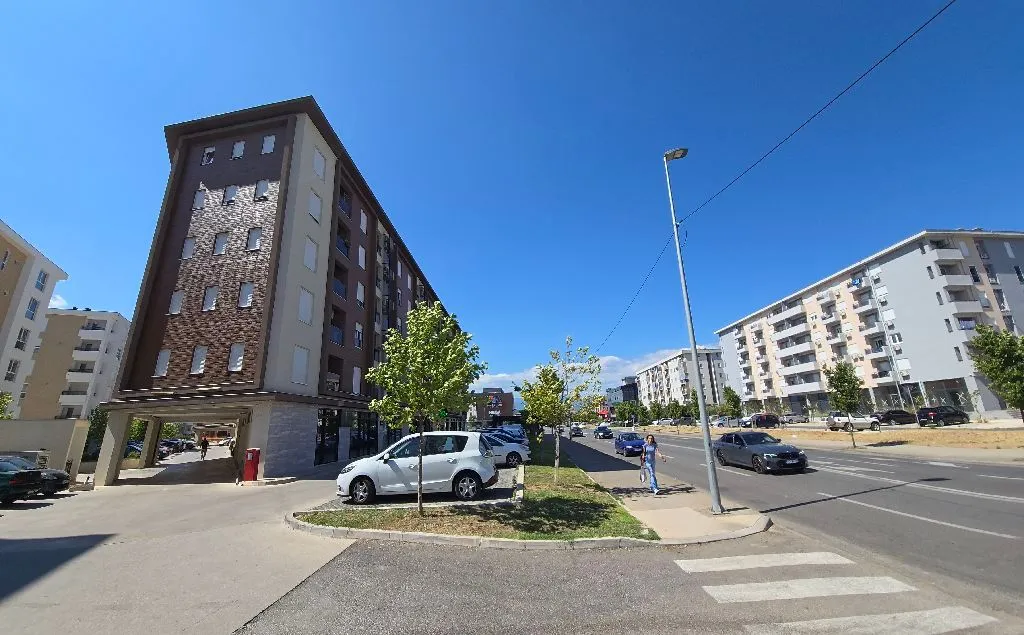 Pogled na stambenu zgradu i ulicu sa parkingom.